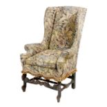 A Queen Anne style wing armchair, upholstered with floral tapestry, on ebonised beechwood scroll