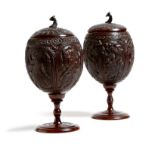 λ Two similar Indian carved coconut cups and covers, each decorated with a peacock and panels of