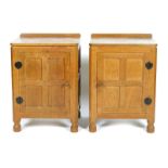 A pair of Robert Mouseman Thompson oak bedside cabinets, with panelled doors and patinated wrought