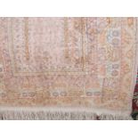 A small woven eastern rug with geometric decoration in shades of pink and lilac upon a cream ground