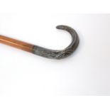 An antique timber walking cane terminating in a crooked handle with applied white metal cap with