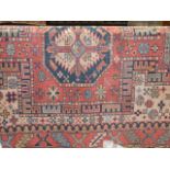 An old eastern woven wool rug with highly detailed decoration, the red ground interspersed with