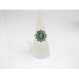 An 18ct gold ring set with ten diamonds around a central oval emerald, size N