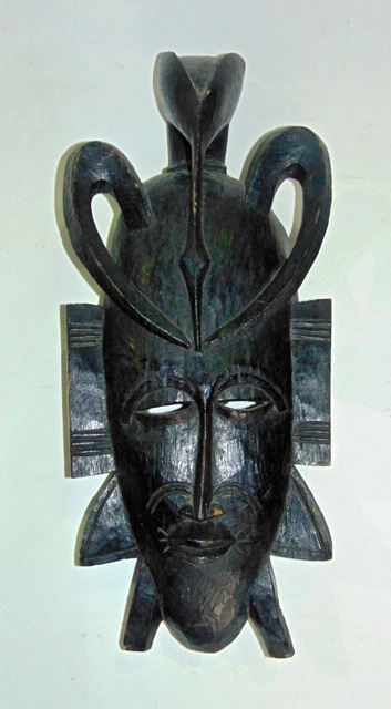 A carved African mask, on the head of which stands a crouching bird