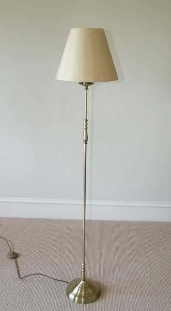 A contemporary standard lamp with brushed brass finish and pale cream conical shaped shade