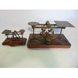 Two vintage brass postal scales of varying size, both raised on wooden platform bases