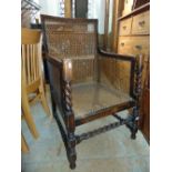 An early 20th century oak framed bergere chair with cane panelled seat back and arms raised on