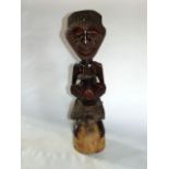 A carved African hardwood songe power figure with applied brass studded detail, snake skin apparel