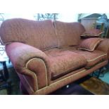 A substantial two seat sofa with scrolled arms and shaped back with deep red upholstered finish