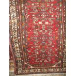 A Persian floor rug decorated with a band of green floral medallions upon a red ground, 155cm x