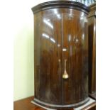 A Georgian mahogany bow fronted hanging corner cupboard with string inlaid detail enclosing three