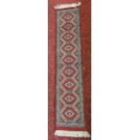 Small Uzbek wool runner decorated with stone coloured medallions upon a red ground, 33cm x 148cm