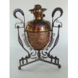 An interesting early 20th century embossed copper oil lamp upon an intricate wrought iron stand,