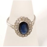 A sapphire and diamond cluster ring in unmarked white metal with central oval cut sapphire and a