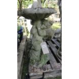 A weathered cast composition stone bird bath in the form of a cherub supporting a shallow circular