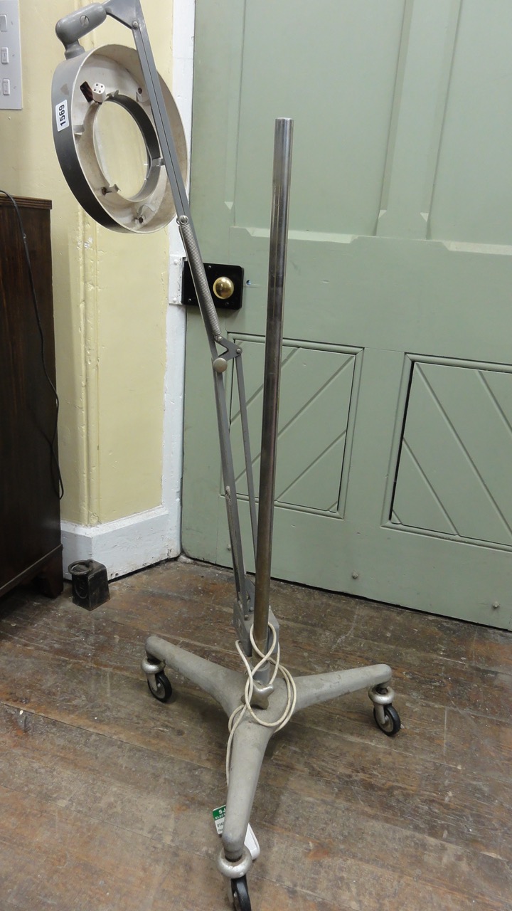 An industrial medical lamp upon a good industrial tripod base fitted with castors.