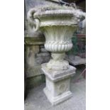 A weathered cast composition stone campana shaped garden urn with ring handles, face mask and