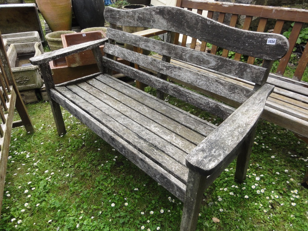 A Swan Hattersley weathered teak two seat garden bench with slatted seat and angled back beneath a