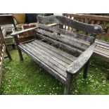 A Swan Hattersley weathered teak two seat garden bench with slatted seat and angled back beneath a