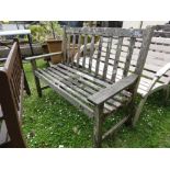 A weathered teak two seat garden bench with slatted seat and back.