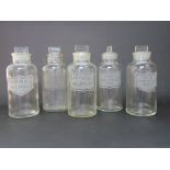 A set of five antique clear glass apothecary bottles with lids.