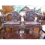 A pair of Chinese hardwood elbow chairs, vigorously carved with wrything dragons amongst clouds,