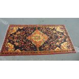 A Persian floor carpet decorated with orange and green medallions upon a deep navy blue ground,