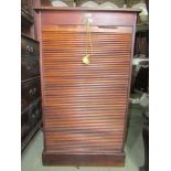 An Edwardian tambour fronted cabinet in oak partially fitted with adjustable shelves 65cm wide.