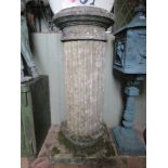 A weathered stone four sectional column with circular cap, fluted pillar and square cut platform