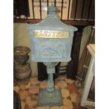 A reproduction painted cast metal floorstanding letter box with simulated tiled roof, crown finial