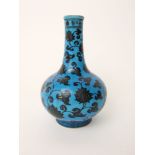 An oriental blue ground bottle shaped vase with dark painted floral and scrolling leaf detail, 21 cm