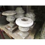 Four small weathered marble urns of varying design but all with square cut bases