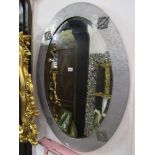 An oval Arts & Crafts style wall mirror with bevelled edge plate within a silver coloured metal clad