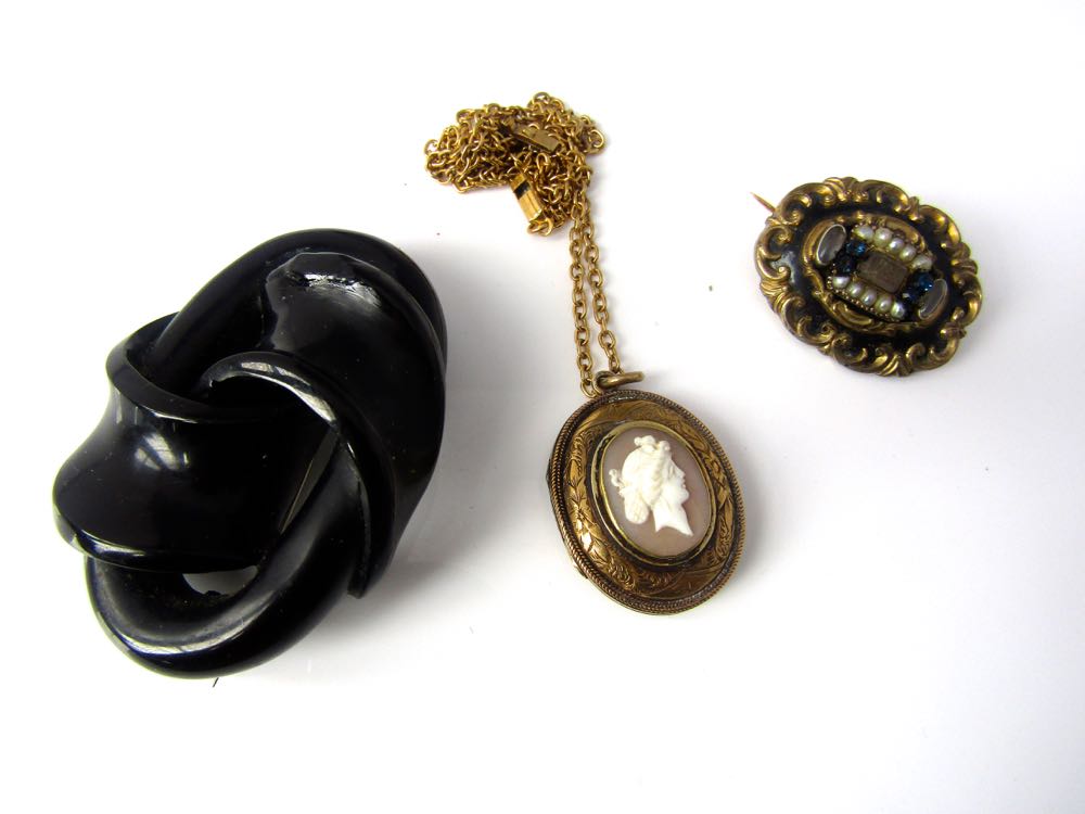 An enamel brooch in scrolling mount, a cameo necklace and a further brooch of knot design