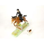 A Beswick model of a huntswoman in black habit on brown horse leaping a fence, with circular printed