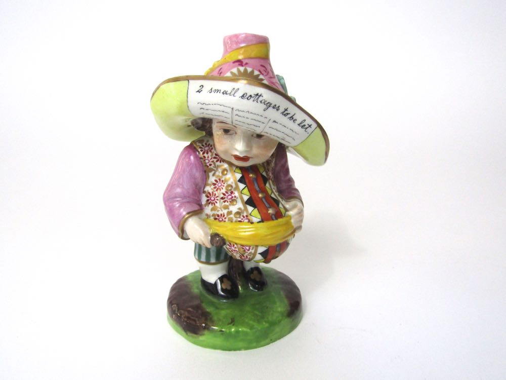 A 19th century figure of a Mansion House dwarf, in the Derby style, wearing a pink hat with yellow