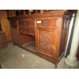 An Edwardian oak sideboard enclosed by an arrangement of cupboards and drawers flanking a central