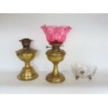 Two similar brass oil lamps, one with cranberry type glass shade together with a further pedestal