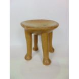 A small African stool with dished seat raised on 4 legs hewn from a single piece of timber with