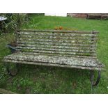 A three seat garden bench with weathered timber slatted seat and combined back rasied on scrolled