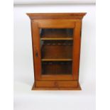 A vintage oak smoker's cabinet with pipe rack and shelves behind a hinged glazed door, above a