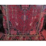 A Persian style wool rug with red field, central medallion and further abstract detail within
