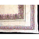 An intricately embroidered table cloth on cream ground with colourful central motif and elaborate