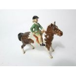 A Beswick model of a little girl in green jacket riding on a brown and white skew bald pony with