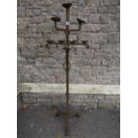 A heavy wrought iron candle stand on three tiers with square cut column and tripod base and with