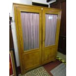 A pale oak freestanding cupboard enclosing three adjustable shelves enclosed by two partially glazed