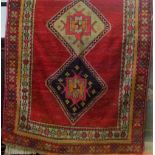 A Turkish wool rug with triple medallion centre upon a red field, within running borders, 230x140cm
