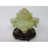 A celadon type jade sensor with two lion head ring handles and pierced dragon lid upon a carved