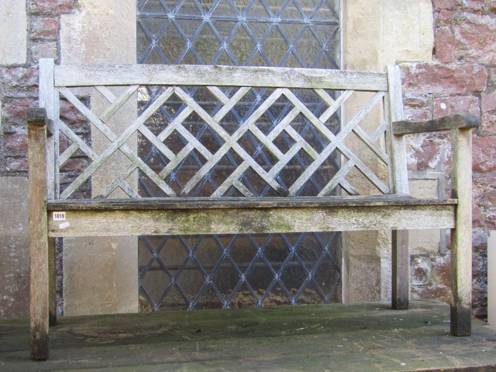 A weathered teak two seat garden bench with slatted seat and decorative lattice panelled back