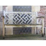 A weathered teak two seat garden bench with slatted seat and decorative lattice panelled back